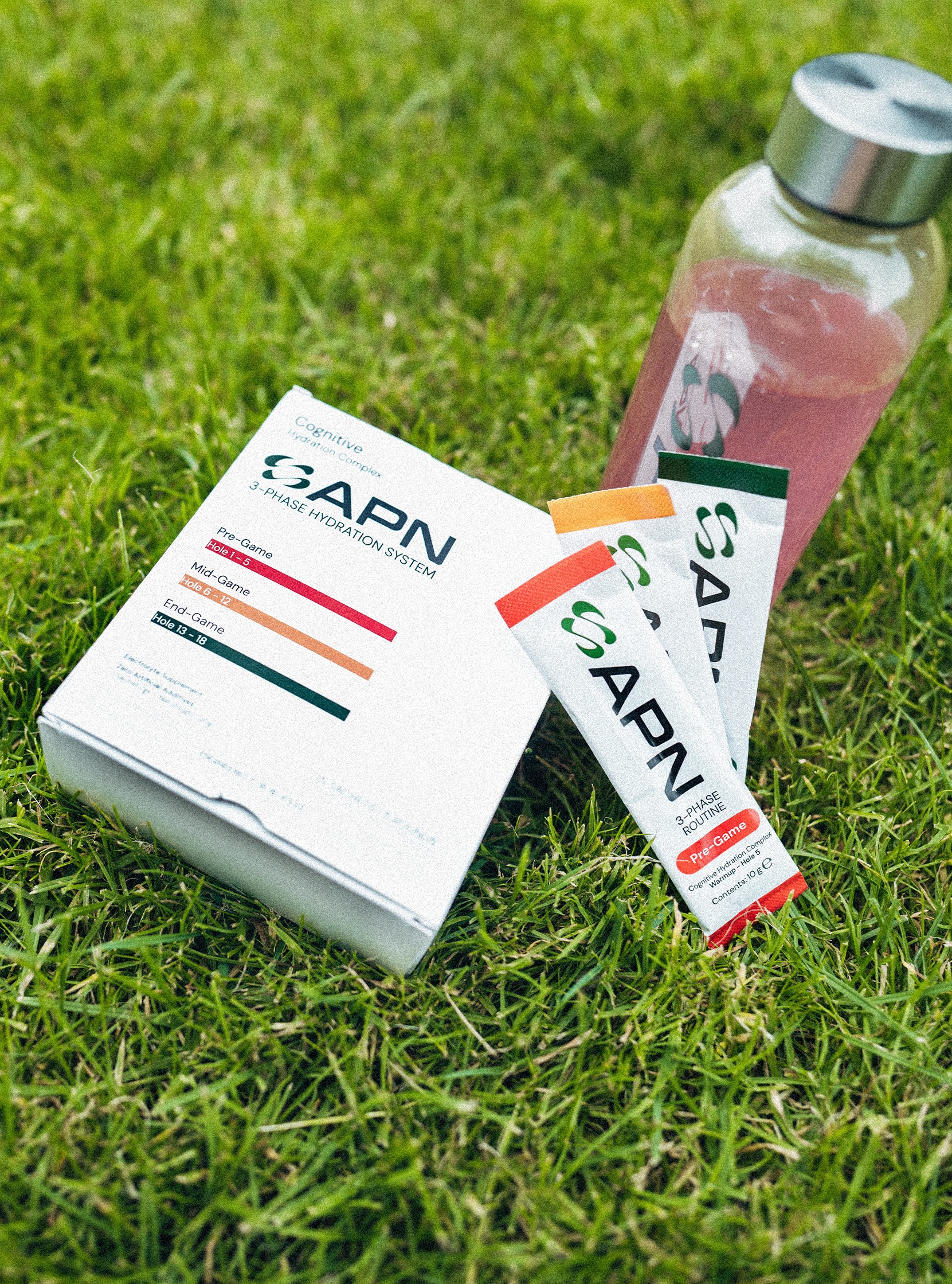 APN 3-Phase Hydration System box on grass with Pre-Game sachets and a drink bottle