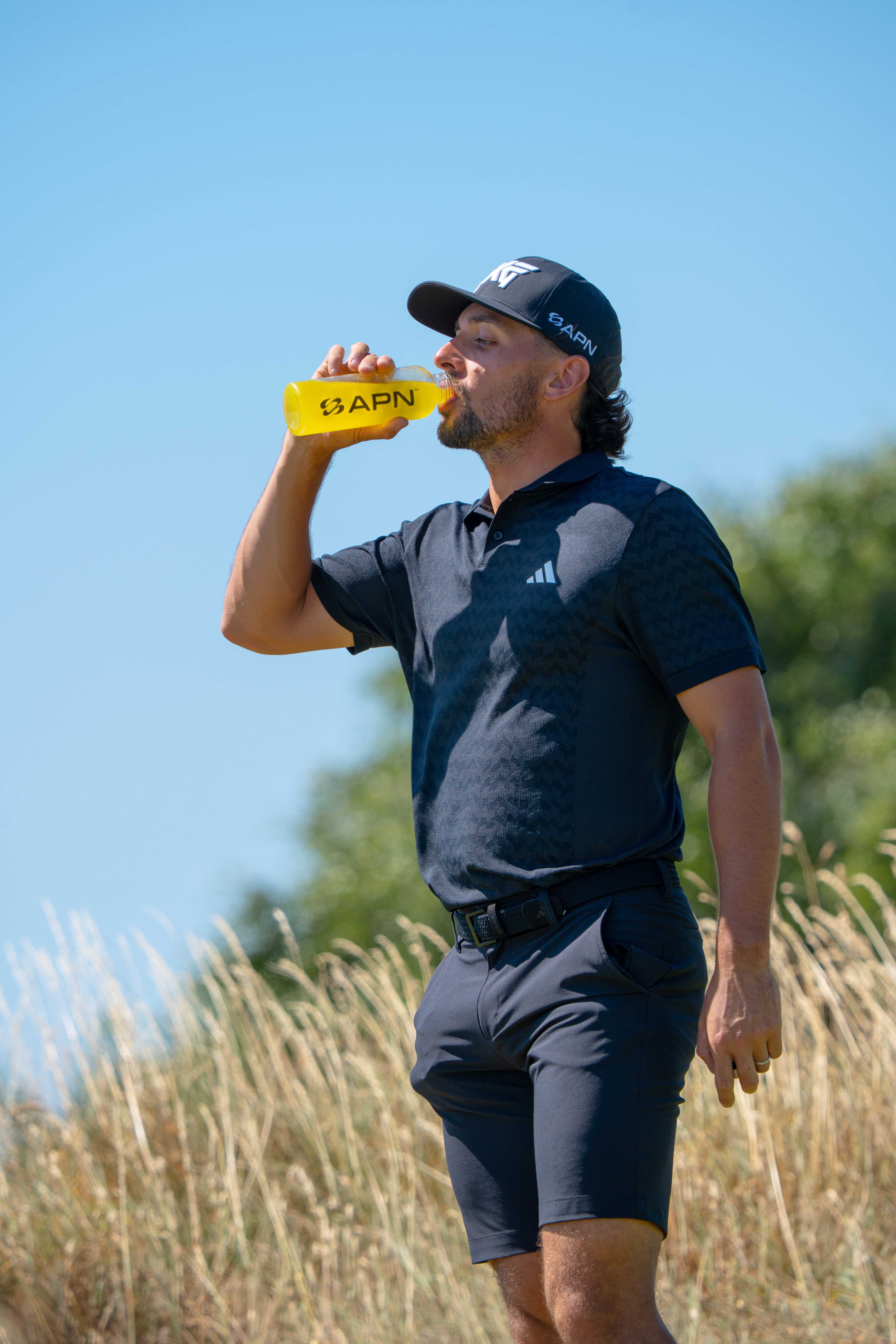Marco Penge drinking from an APN FUEL bottle in tall grass