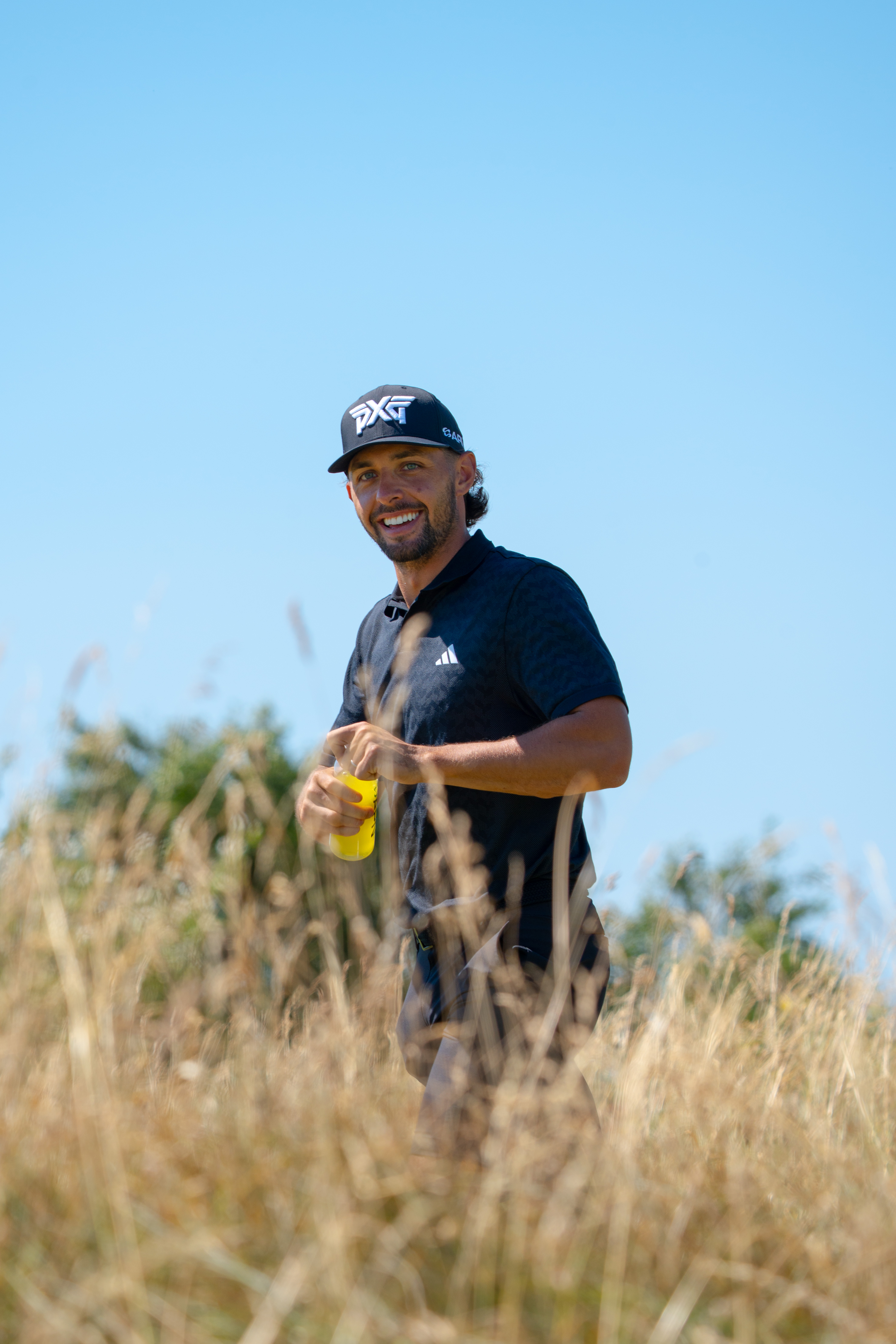 Marco Penge holding an APN FUEL bottle while walking through tall grass