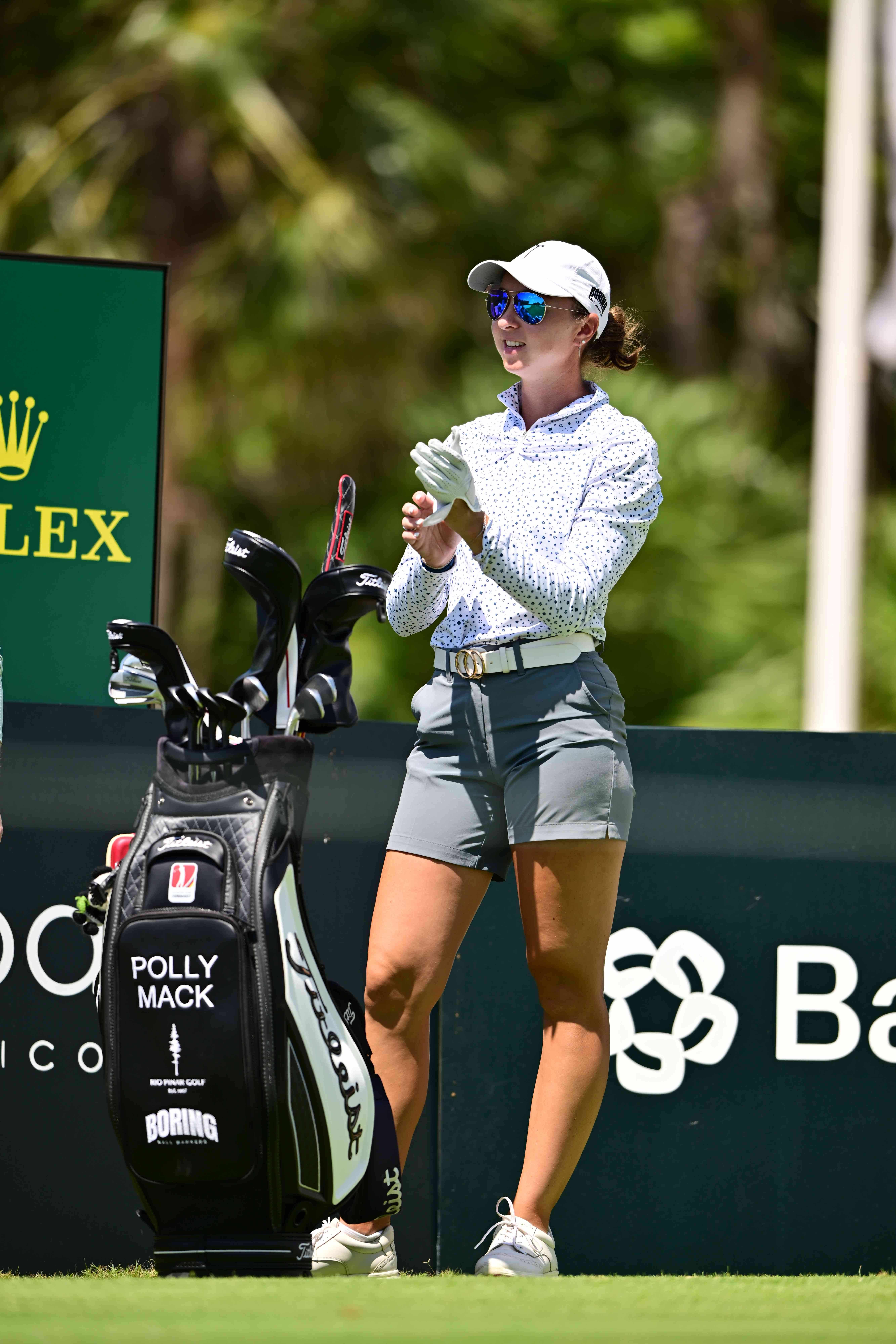 Polly Mack pulling on her glove beside her Titleist bag on the tee