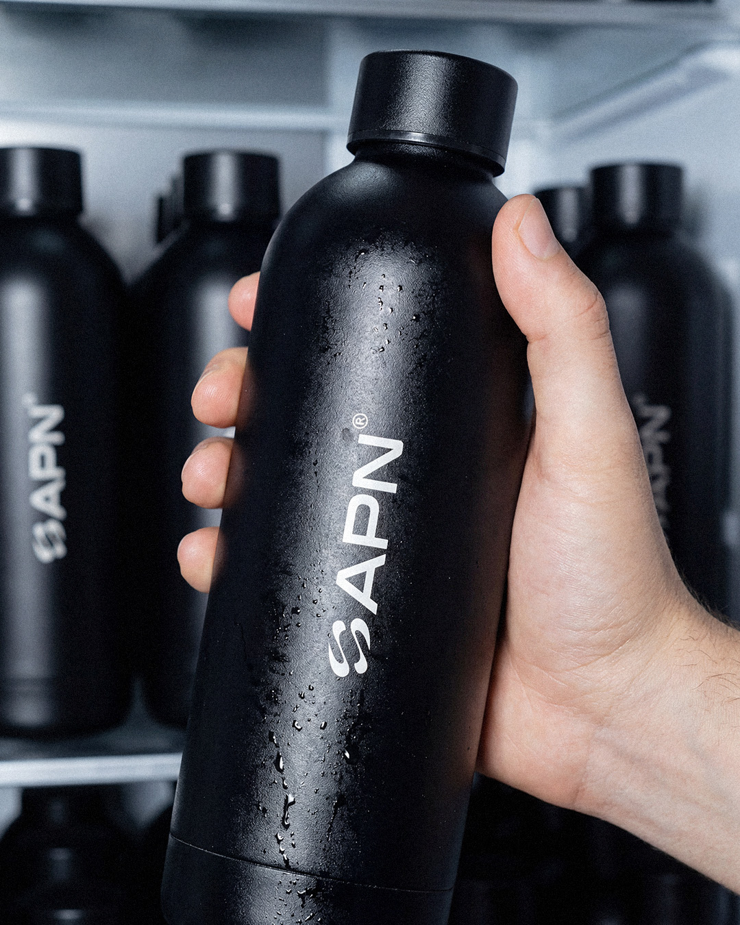 APN Thermo Water Bottle — held in hand, fridge background