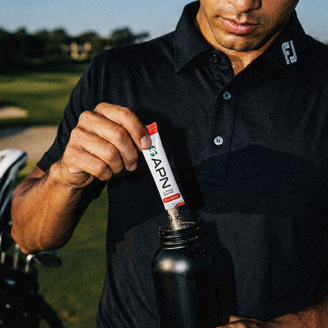 Golfer pouring an APN Pre-Game sachet into a black APN bottle on the course